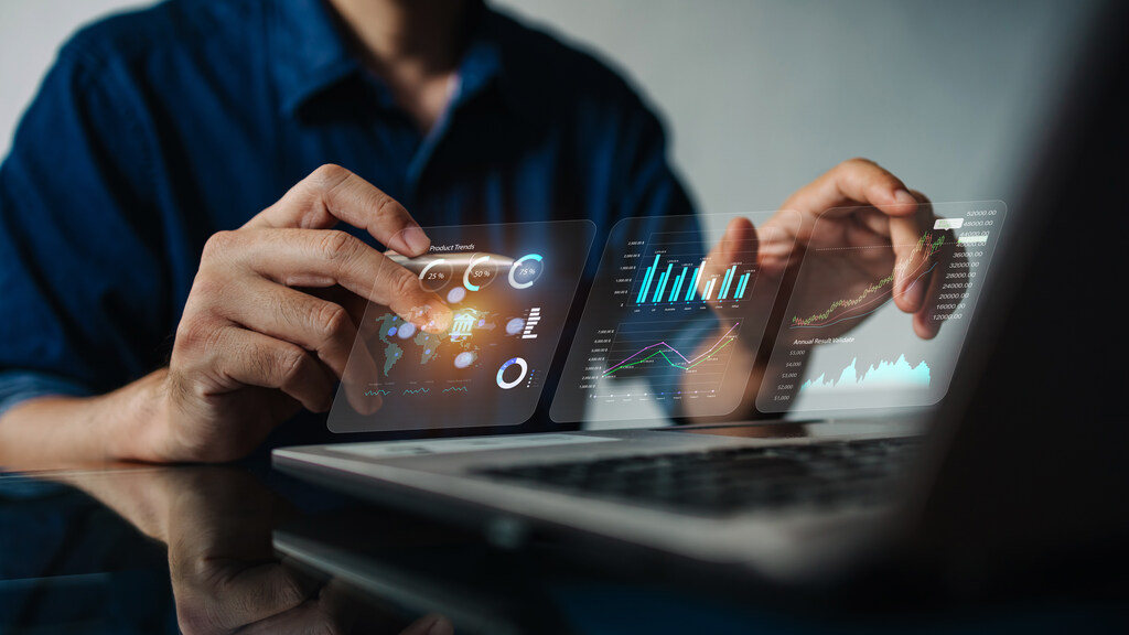 Homem trabalha em seu computador, e imagens holográficas ilustram a sua atividade focada em análise de dados em um ambiente corporativo futurista.